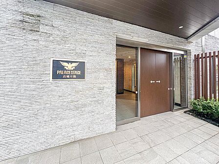 「PALACESTAGE 高幡不動」の看板が迎える、洗練されたエントランス。白い石積みの壁とモダンなドアが、家族の帰りを温かく包み込みます。