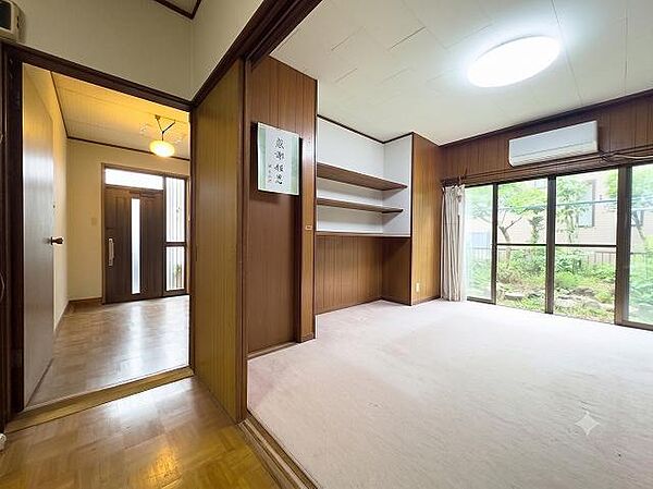 玄関から続く明るい空間は、家族を温かく迎え入れます。隣接する部屋の棚は、お子様の成長に合わせて多目的に活用可能。窓から緑が広がり、開放感あふれる住まいです。