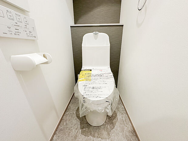 背面のダークカラーが空間を引き締める、清潔感のあるトイレ。温水洗浄機能付きで、毎日を快適にサポートします。上部の棚には消耗品などをすっきり収納できます。