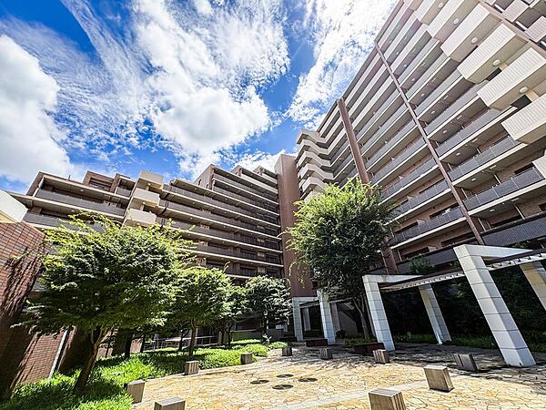 青空の下、緑豊かな広場が広がるマンション外観。お子様がのびのびと遊べるスペースがあり、家族の笑顔が溢れる毎日を育みます。