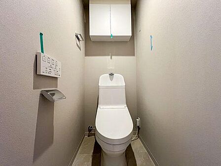 清潔感のある温水洗浄便座付きトイレ。上部にはトイレットペーパー等を収納できる吊戸棚を備えています。