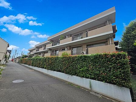 道路側から建物全体を見渡せる外観です。3階建ての低層レジデンスは、各階に連なるバルコニーと植栽が調和した佇まい。敷地沿いには豊かな緑が配置され、周辺の落ち着いた住宅街にも自然に馴染む住環境です。