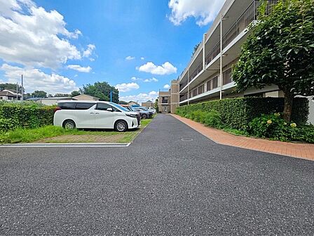 敷地内には平置きの駐車スペースが設けられ、建物までのアプローチにもゆとりが感じられます。周囲には植栽が配置され、駐車場と住棟の間にも歩行スペースを確保。日々の車の出入りもしやすい敷地配置です。