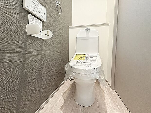 ダークグレーのアクセントクロスがおしゃれで落ち着いた雰囲気を演出するレストルーム。手洗い付きの温水洗浄便座を完備し、奥の棚には小物も飾れる快適で清潔感あふれる空間です。