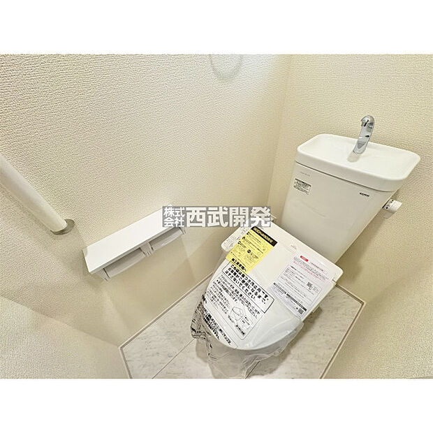 白で統一された清潔感のある温水洗浄機能付きトイレ。手すりもあるバリアフリー設計です。