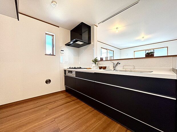 ~キッチン~・同仕様・ 温かみのある床材と、都会的なデザインのキャビネットが調和する、洗練された空間。窓から見える空が、日々の暮らしに心地よい彩りを添えます