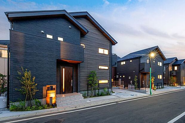 【　住協建設の施工例　】黒の木目調が織りなす重厚な佇まい。 洗練されたダークトーンの質感が夕暮れの街並みに美しく映える、デザイン性の高いモダン邸宅。
