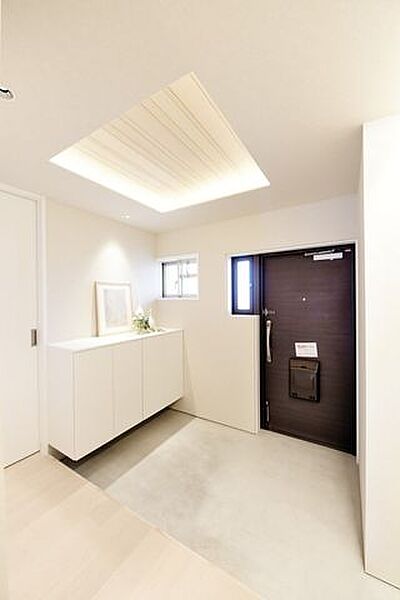 玄関から住まいのコンセプトを感じられる設計。無垢突板材をあしらった折り上げ天井と間接照明が奥行きを演出し、住戸の奥へと自然に視線を導きます。上質な素材感と開放感が調和した、印象的なエントランス空間です
