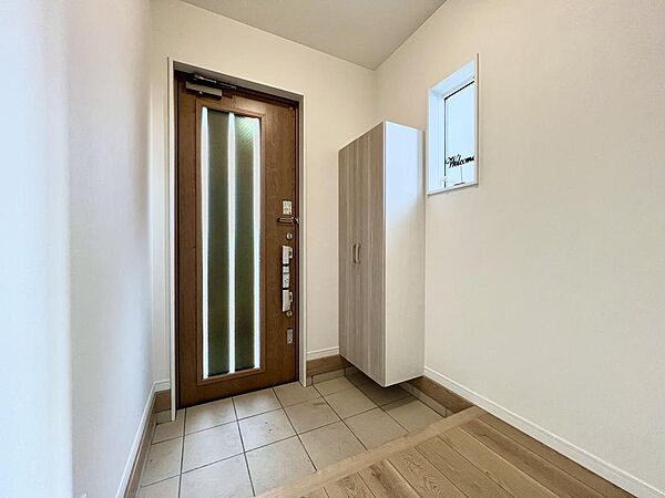 温かみのある木目調のドアと、清潔感のある白い壁が調和した、心地よい第一印象を与える玄関スペースです
