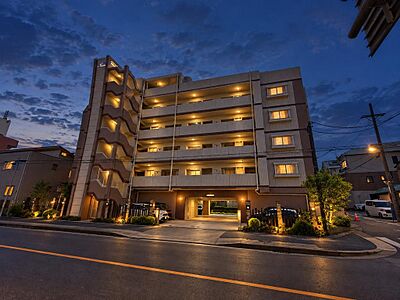 外観：6階建てのマンションを見上げる夜景です。エントランス照明が灯り、帰宅時も落ち着いた雰囲気です