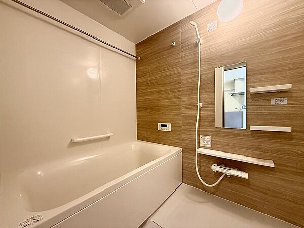 木目調のパネルと大きな鏡を配したユニットバスです。壁面の給湯パネルで湯温を調整でき、ホテルの客室のような寛ぎの時間を過ごせます