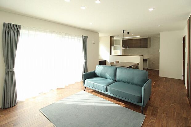 南からの採光で室内は明るくLDK18帖の広さ。室内にあるカーテン、照明、家具はそのままのお引き渡し。床材もシックな色合いで落ち着いたリビングになっています。