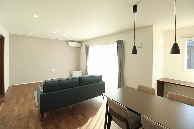 リビング全体。南からの採光で室内は明るくLDK18帖の広さ。室内にあるカーテン、照明、家具はそのままのお引き渡し。床材もシックな色合いで落ち着いたリビングになっています。