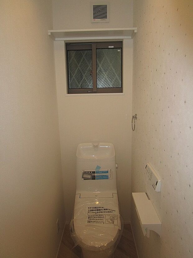 １階のトイレ：温水洗浄便座付きのトイレです。上部に収納棚があり便利です。換気扇や窓があります。