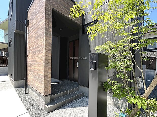 木目調のドアとグレーの外壁が調和したダブルロックの玄関。宅配BOXつき