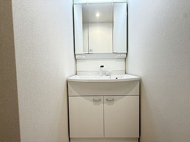 【洗面化粧台】ホワイトで統一された清潔感溢れる洗面所に、三面鏡仕様の洗面化粧台が設置されています。