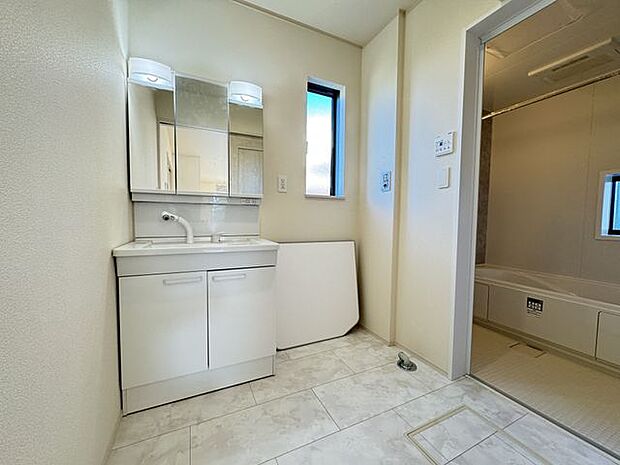 【洗面室】身支度に重宝する、ライト付き三面鏡仕様の洗面化粧台が設置されています。洗濯機置場には小窓付き。