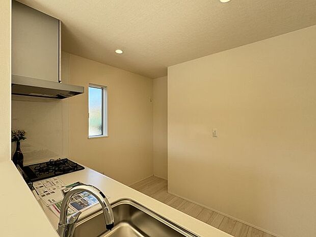 【キッチン/1号棟】対面キッチンからリビングにいるご家族を見守れる設計です。西側に窓が設けられており、調理中も自然換気が可能。