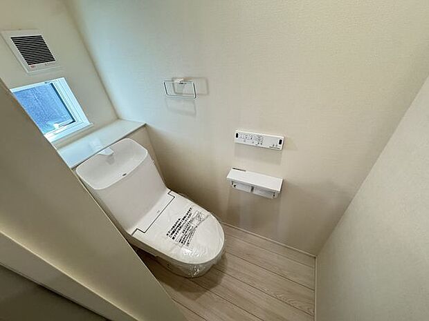 【1階トイレ/1号棟】自然光が入る窓付きトイレです。温水洗浄便座が備わり、寒い時期でも快適に使用できます。操作しやすい壁面リモコンが採用されています。