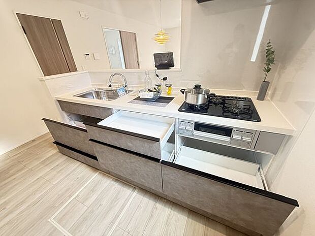 【1号棟/キッチン】コンロは並行調理ができる三口タイプ。グリルも合わせて活用することで、調理の効率化と時短が叶います。※家具調度品等は販売価格に含まれません。