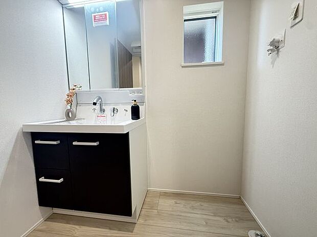 【1号棟/洗面室】身支度に便利な三面鏡付きの洗面化粧台。洗面ボウル下に収納スペースが備わり、タオルや小物などを整理できます。洗面化粧台の横には洗濯機を設置するスペースが設けられています。