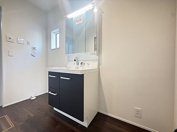 【2号棟/洗面室】身支度に便利な三面鏡付きの洗面化粧台。洗面ボウル下に収納スペースが備わり、タオルや小物などを整理できます。洗面化粧台の横には洗濯機を設置するスペースが設けられています。