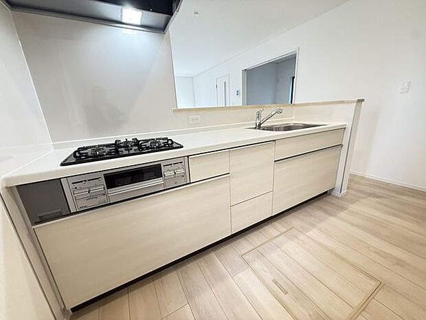 【キッチン/3号棟】ガスコンロは、並行調理が可能な三口タイプ。キッチン前面に腰壁があり、手元部分がリビング側から見えにくい設計です。奥の物を出し入れしやすいスライドタイプの収納が採用されています。