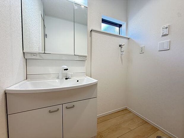 【洗面室/4号棟】朝の身支度をスムーズに行える三面鏡仕様の洗面化粧台。鏡裏や洗面ボウル下部に収納スペースが設けられています。洗面化粧台の隣に洗濯機置場が設けられています。