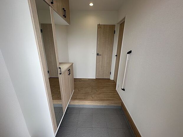 【玄関/4号棟】大型の下駄箱には身だしなみチェックに便利な姿見が備え付けられています。手すりが設置されており、小さなお子様やサポートが必要なゲストにも安心です。