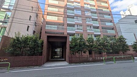 レンガ調の外壁と植栽が並ぶ建物前。歩道状のスペースが整えられており、駅や街から帰宅する時間も住まいへ向かう小さな楽しみになりそうです♪