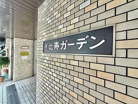 【エントランス】重厚感のあるタイル壁に美しく映える、モダンなデザインのマンションサイン。