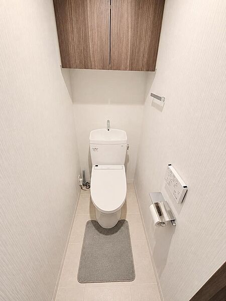 温水洗浄機能付きトイレを採用。上部には扉付きの収納棚を備えており、トイレットペーパーや清掃用品などをすっきり収納できます。落ち着いた木目調の収納と明るい内装が調和した、清潔感のある快適な空間です。