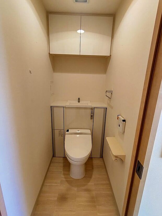 トイレの写真です。温水洗浄機能付きトイレです。吊り戸棚があり備品の収納がすっきり片付きます。