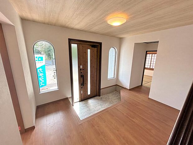【リフォーム済】玄関の写真です。玄関ドアは新しいモノと交換いたしました。木目調のドアと天井のクロス、窓からの採光がぬくもりのある空間を演出してくれていますね。アーチ状の窓がアクセントになっております。