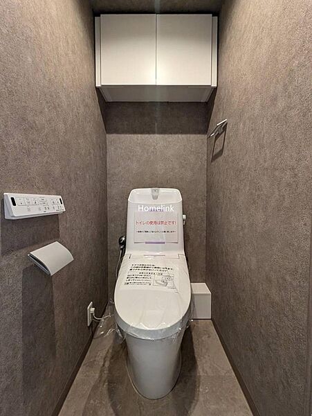 【トイレ】ウォシュレット付きのトイレです。お掃除のしやすいタンク一体型の便器で、操作のしやすい壁リモコン仕様。上部には吊戸棚で収納も確保しています。