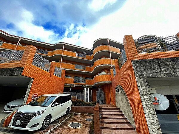 青空に映えるオレンジ色の外壁が特徴的なマンション。駐車場も完備しており、快適な暮らしをサポートします。