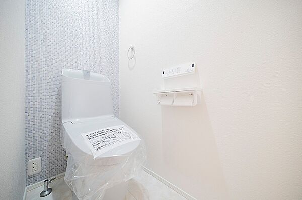 淡いブルーのモザイクタイルが印象的なトイレ空間。清潔感あふれるホワイトで統一され、快適なひとときを演出します。快適な暮らしを支える設備が整っています。