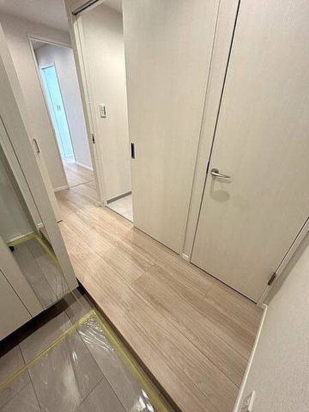 白を基調とした建具と温かみのある木目調のフローリングが特徴的な玄関で、姿見付きの収納や複数の居室へ繋がる扉、奥には床タイル仕様のスペースなど機能的な動線が確保されています。