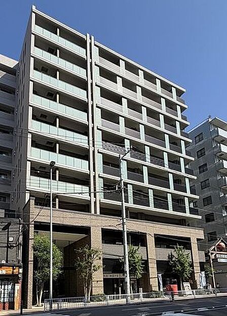 低層部にシックなタイル調デザインを採用し、上層部にはガラスパネルや格子の手すりを配したモダンな佇まいのマンションで、エントランス周辺には綺麗に整えられた植栽が配置されています。
