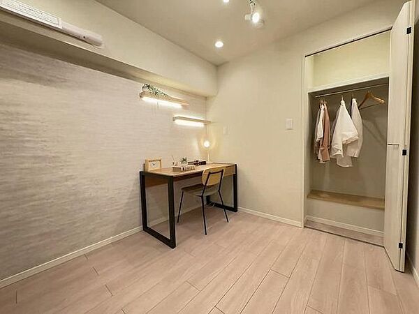 明るい木目調のフローリングが施された洋室には、ハンガーパイプを備えた収納が付いており、壁面にはアクセントクロスや照明付きの飾り棚、天井にスポットライトが設置されております。