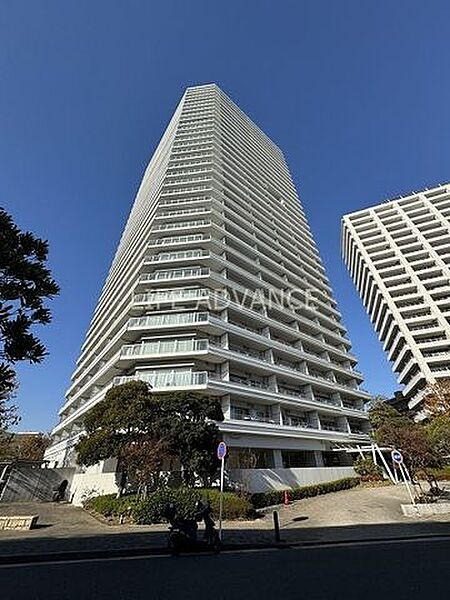 白を基調としたスタイリッシュな外観デザインの高層マンションで、各階にはガラス調の手すりを備えたバルコニーが設けられており、敷地周辺には緑豊かな植栽や整えられたアプローチが配置されています。