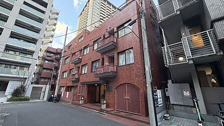 赤茶色のタイル貼りが特徴的な外観デザインで、エントランス部分には庇や数段のアプローチ階段が施されているほか、各階にはバルコニーや開口部が配置されています。