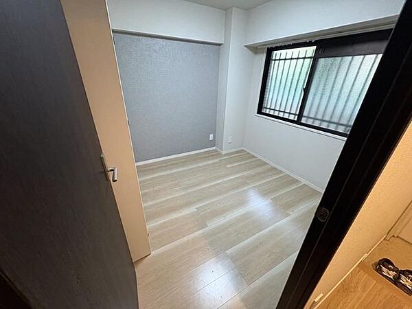 温かみのある木目調のフローリングが施工された洋室には、壁一面に落ち着いたグレーのアクセントクロスが施されており、外側に面格子を備えた腰高窓が設置された造りとなっています。