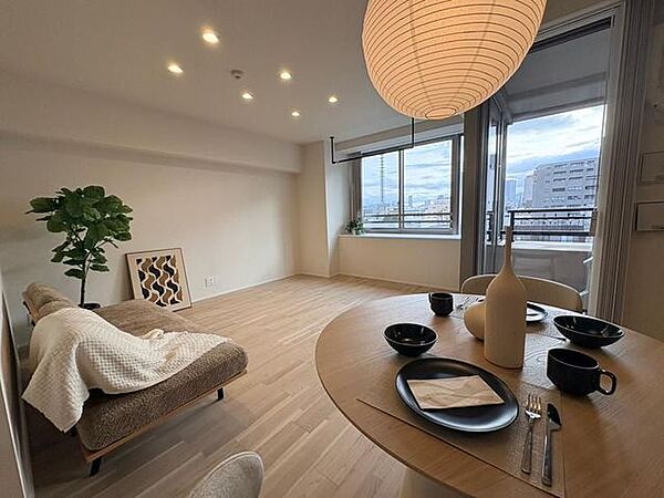 ナチュラルな木目調フローリングと白いクロスで仕上げられた室内には、天井に複数のダウンライトや室内干しに役立つハンガーパイプが設置されており、バルコニーに面した大きな開口部が備わっています。