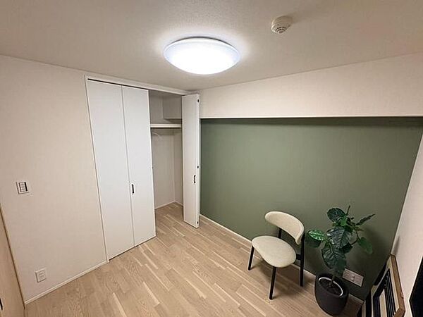 落ち着いたグリーンのアクセントクロスが印象的な室内に、ハンガーパイプと上部棚が付いたクローゼットを完備しており、ナチュラルな木目調フローリングとシンプルなシーリング照明が備わっています。
