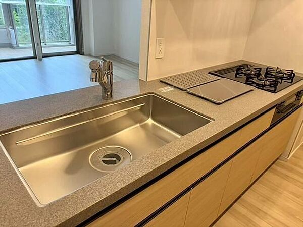 木目調のデザインが施された対面式のシステムキッチンには、3口ガスコンロやグリル、シンク、浄水器一体型水栓が備わっており、天板には質感のある石目調の素材が採用されています。