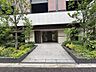 エントランス：アプローチの両脇には青々とした植栽が整然と配されており、フラットなタイル敷きの通路を進むと、シックな縦格子デザインが施されたガラス扉のエントランスへとつながっています。