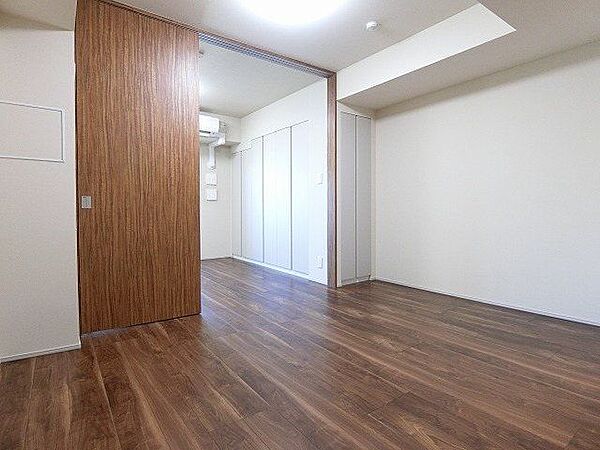 木目調のフローリングと白いクロスを採用した洋室には、隣室との間を仕切ることができる大型の引き戸が備わっており、奥の壁面にはフラットなデザインの作り付け収納が設置されています。