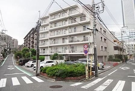 白を基調とした外壁に各階バルコニーが配置されたマンションで、角地に位置し敷地内には駐車場や植栽スペースが整備されています。