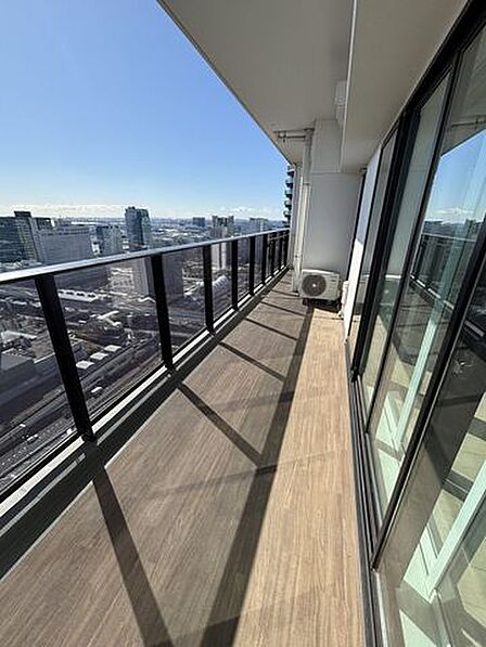 木目調のシートが敷かれたバルコニーには、ガラスパネルの手すりが採用されており、室内からは幅の広い引き違い式の大きなサッシ窓を通って出入りできる造りになっています。